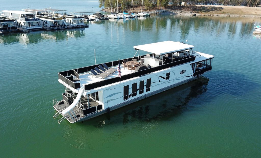 A large black and white houseboat in a port on a green-blue lake. This image is a listing from Big Creek Marine Group